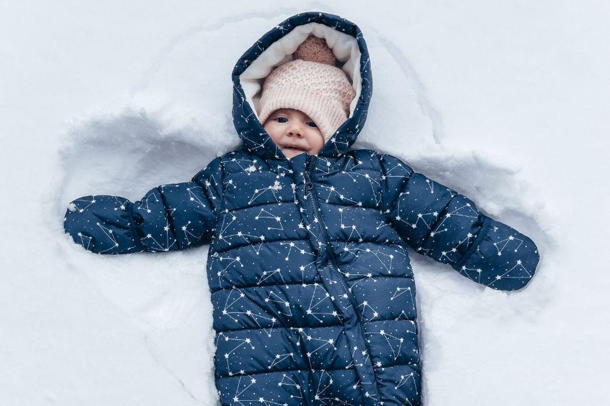Baby in blue snowsuit lying in the snow