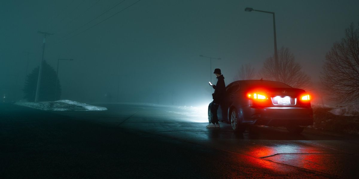 man in black jacket and black pants standing beside red car during night time