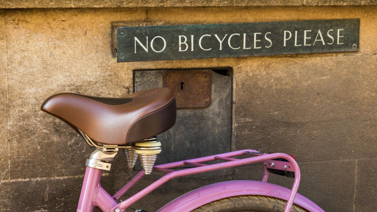 pink bicycle parked beside brown concrete wall with "no bicycles please" sign
