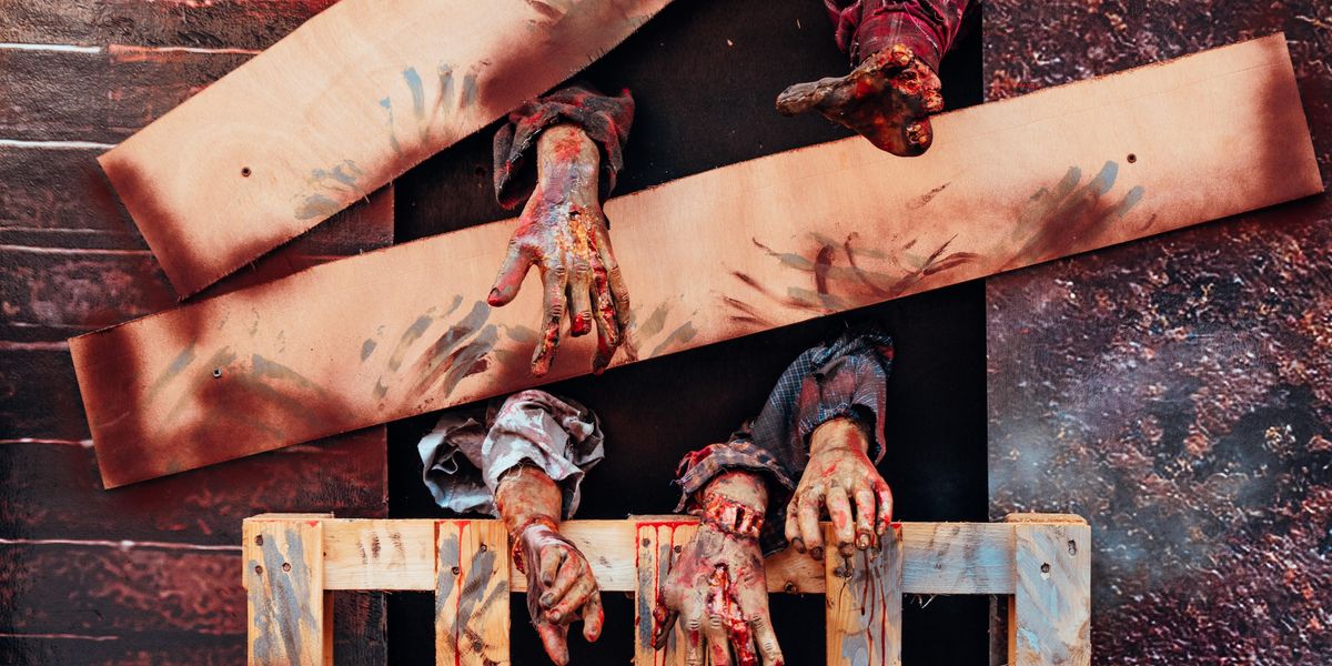 bloodied zombie arms reach out from behind wooden barrier