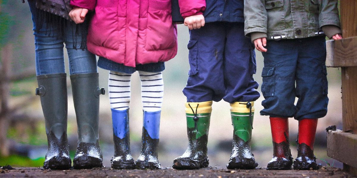 muddy boots and legs visible of four children standing on dirt