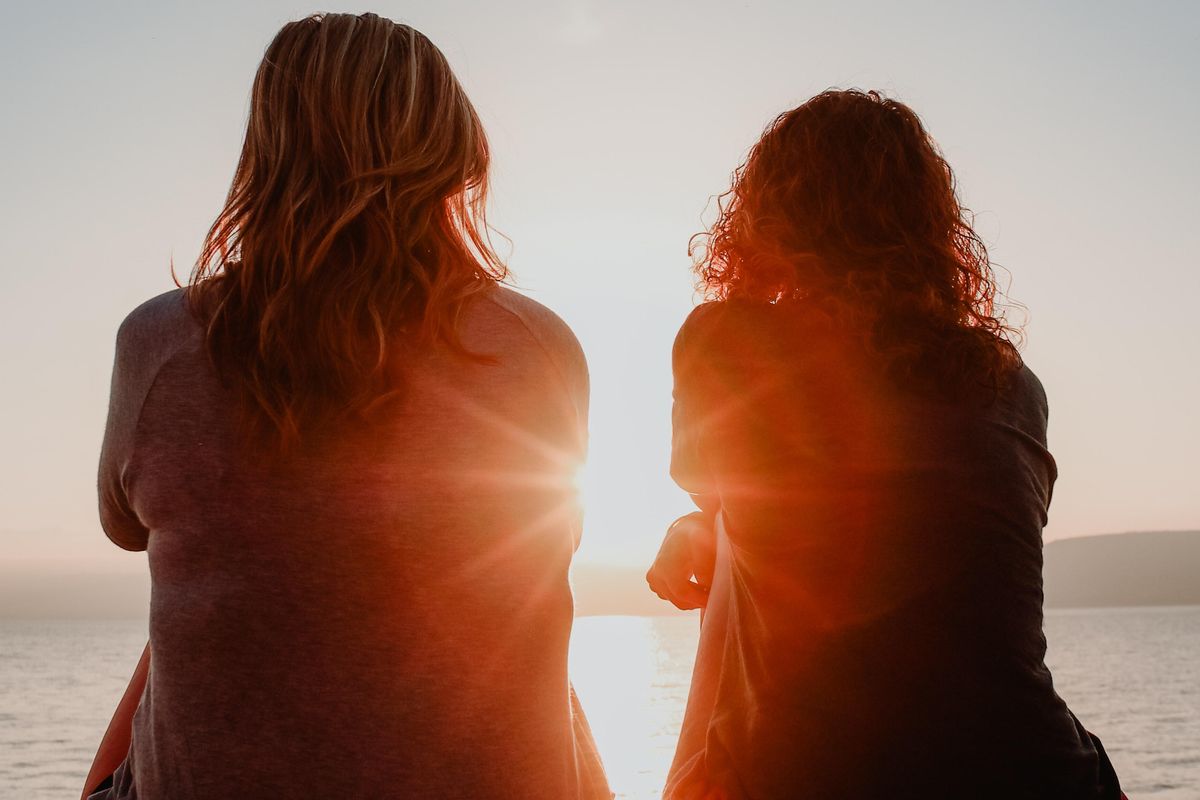 two women sitting on beach facing ocean sunset