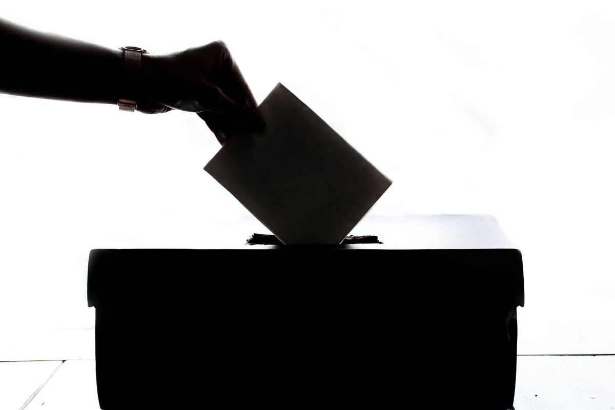 Black and white picture of someone putting a ballot in a box.