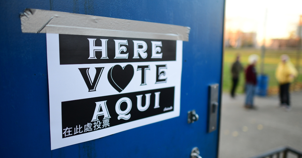 sign taped on blue door with "vote here" printed in multiple languages