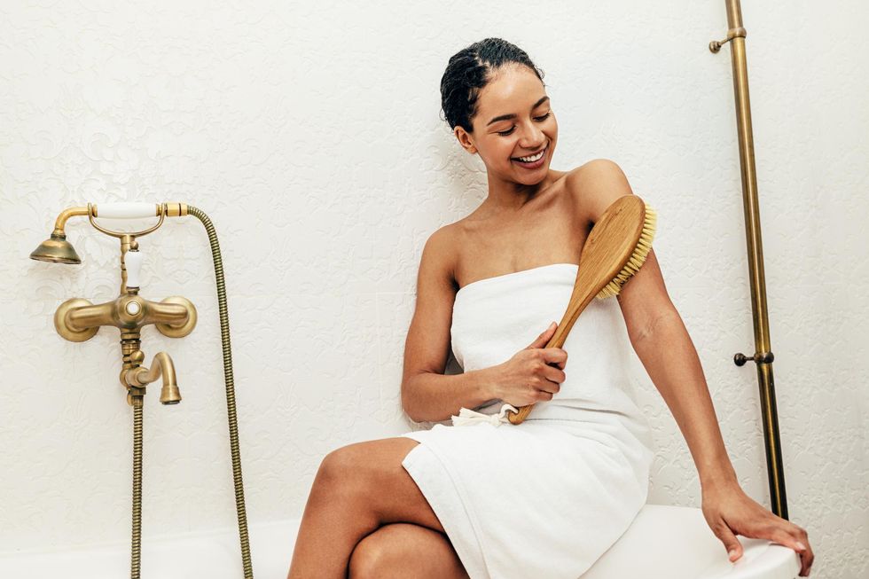 Black woman sitting in a bathtub brushing her skin with dry brush
