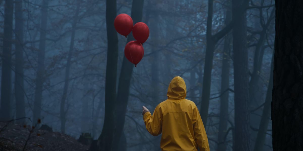 Person holding red balloons in a dark forest