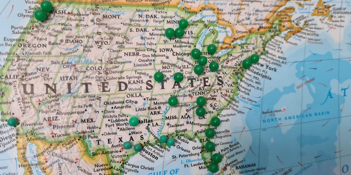 A map of the USA with green thumbtacks sticking in certain cities
