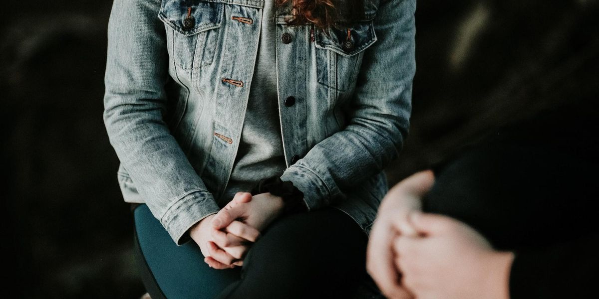 A woman with clasps hands sits across from her therapist