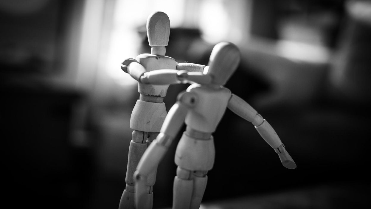 A black and white photo of two wooden toys, one strangling the other