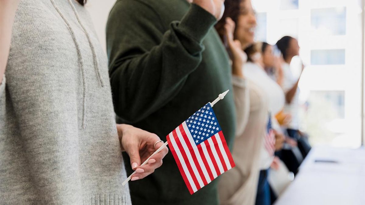 A diverse group of people stand holding small U.S. flags and taking an oath.