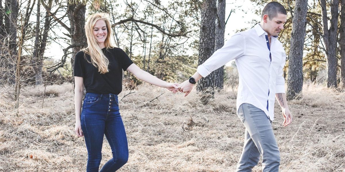 A man and woman walk through the woods holding hands