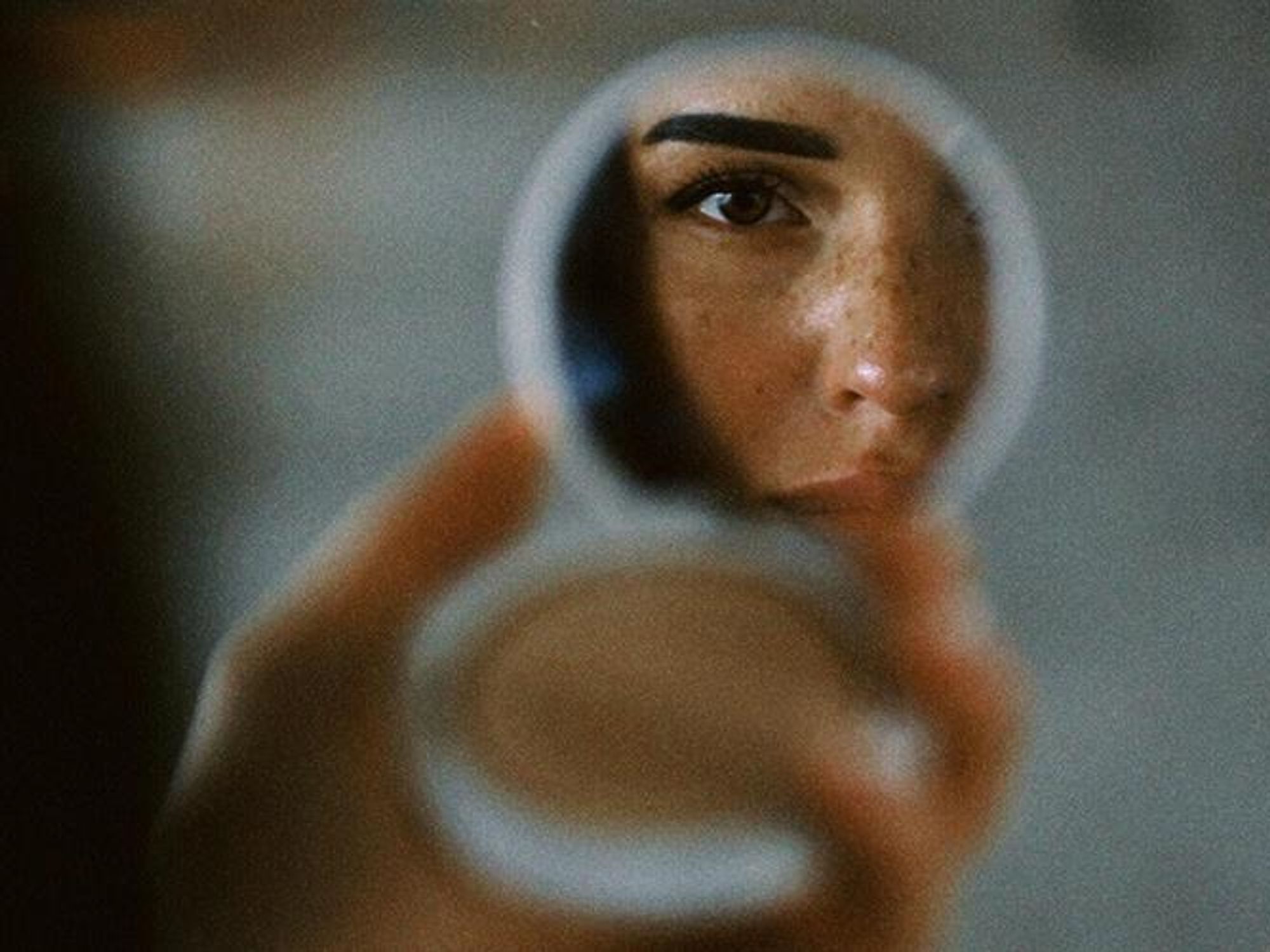 a woman looks at her reflection in a hand mirror