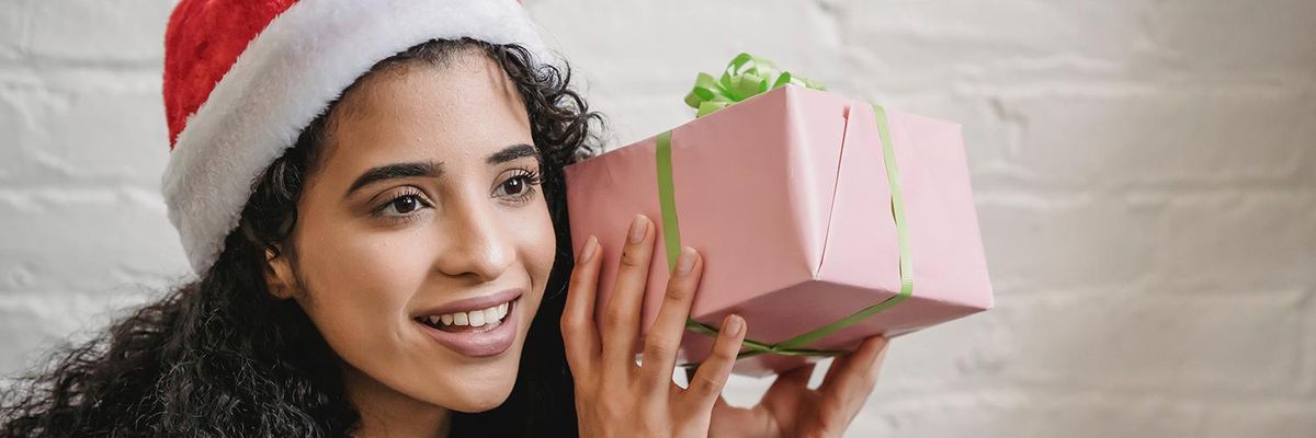 The Ultimate 2022 Latine-Owned Gift Guide latina girl wearing a santa hat with a pink and green gift box in her hands 
