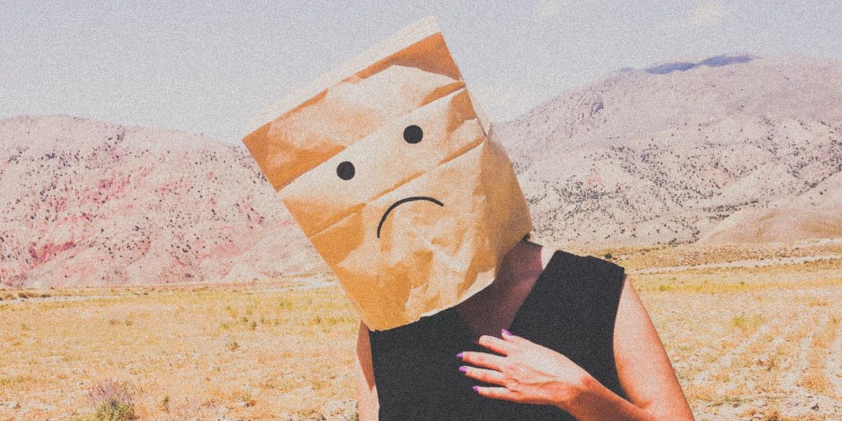 person in black dress wearing sad face brown paper bag on their head