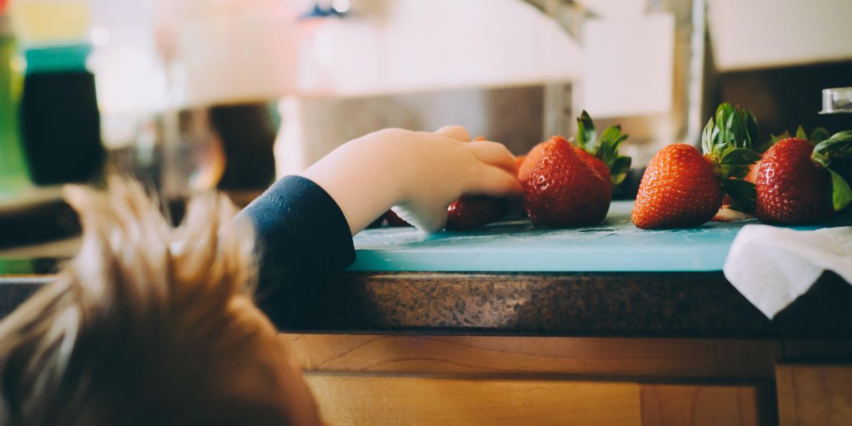 Kid reaching for a strawberry on the kitchen countertop