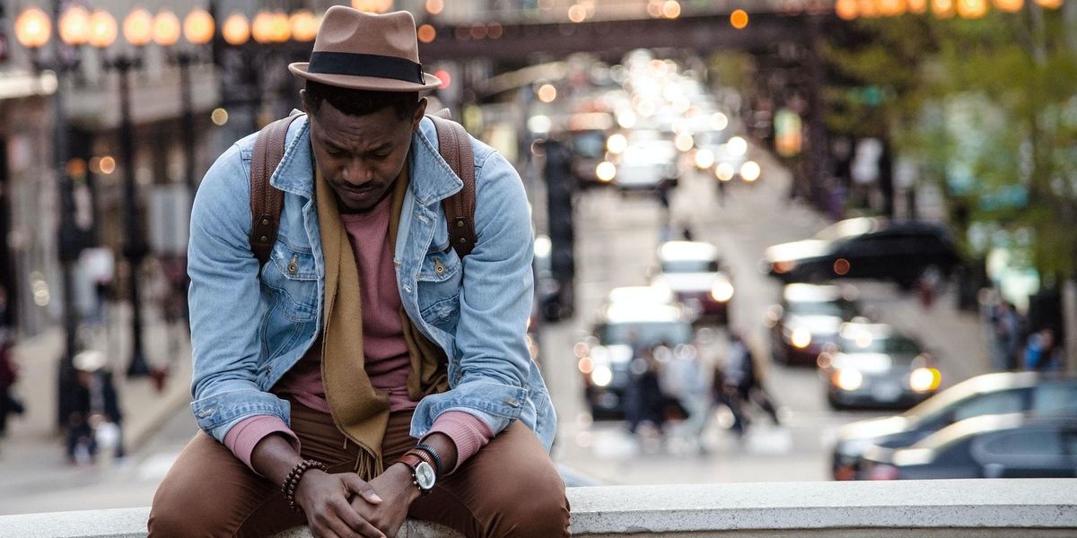 A man sits with a forlorn look while the blurry city bustles behind him