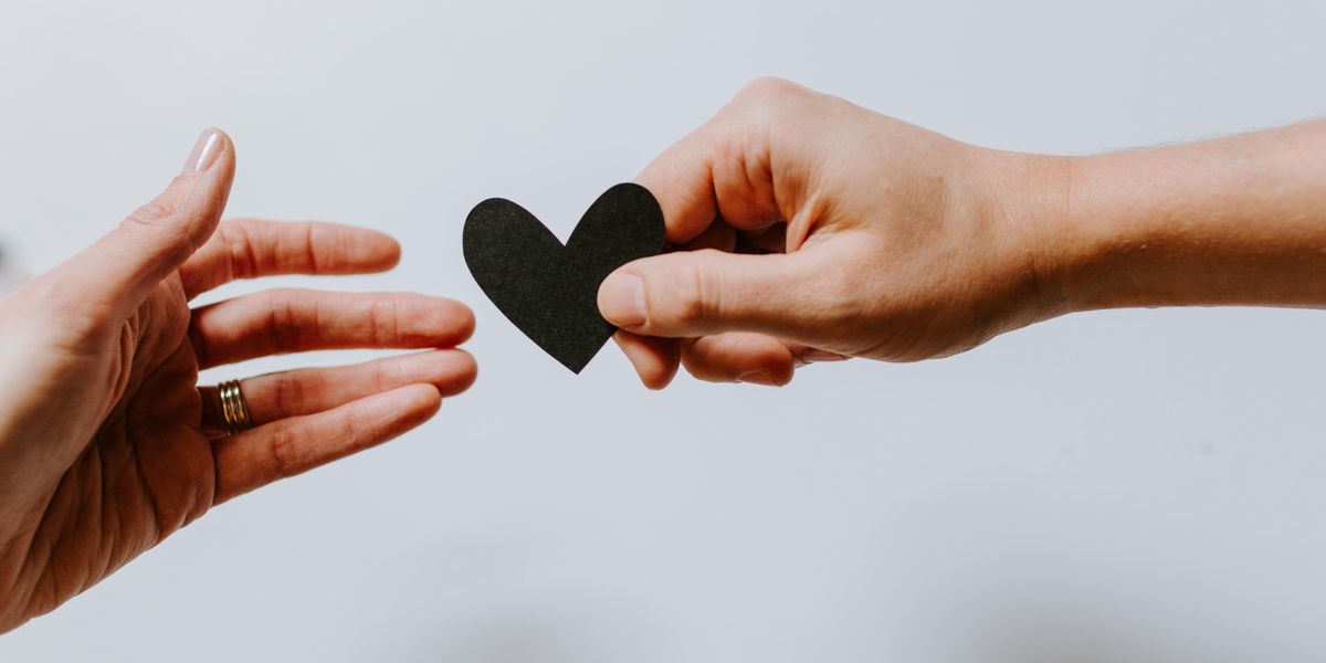 Person symbolically offering a paper heart to someone else