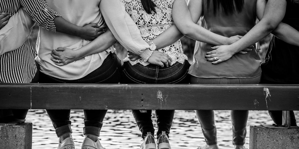 Several people sit on a bench holding one another