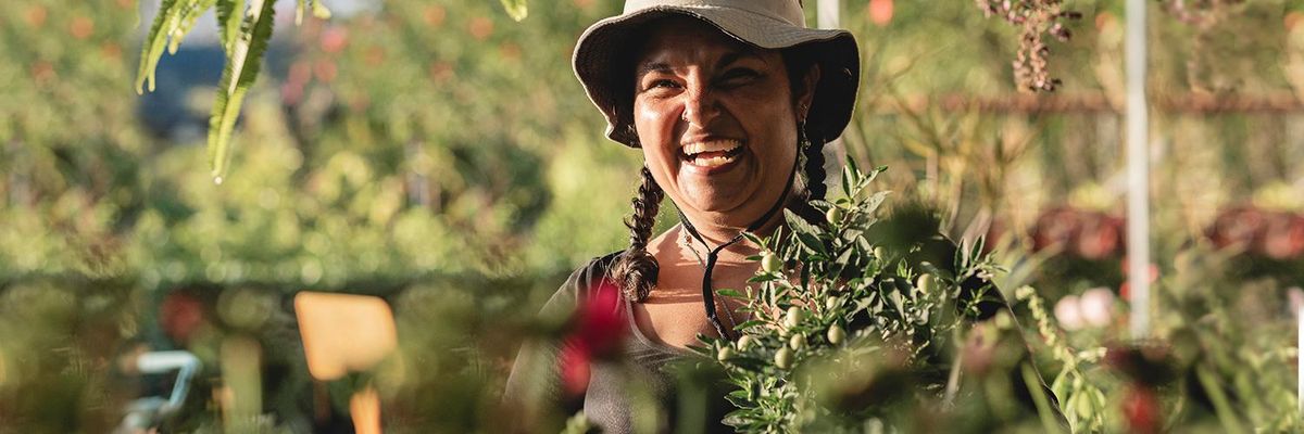 latina middle aged woman wearing hat smiling inside a greenhouse