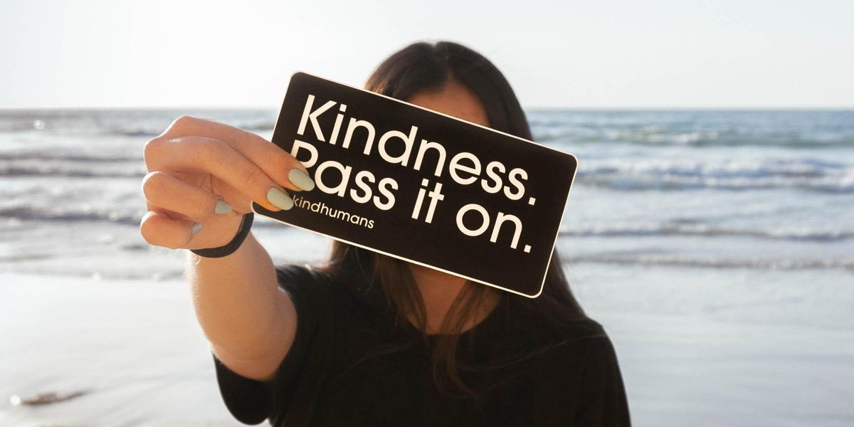 Woman holding sign that reads, "Kindness. Pass It On."