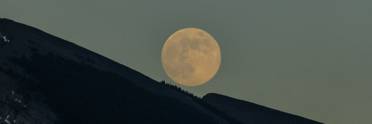 a full moon above the dark silhouette ridge of a mountain