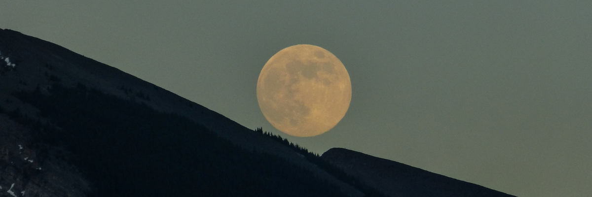 a full moon above the dark silhouette ridge of a mountain 