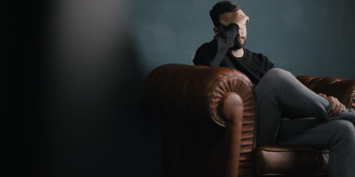 a man holds his head while sitting on a sofa