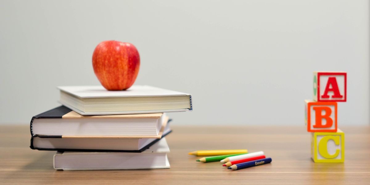 Books, red apple, and toys on elementary school teacher's desk