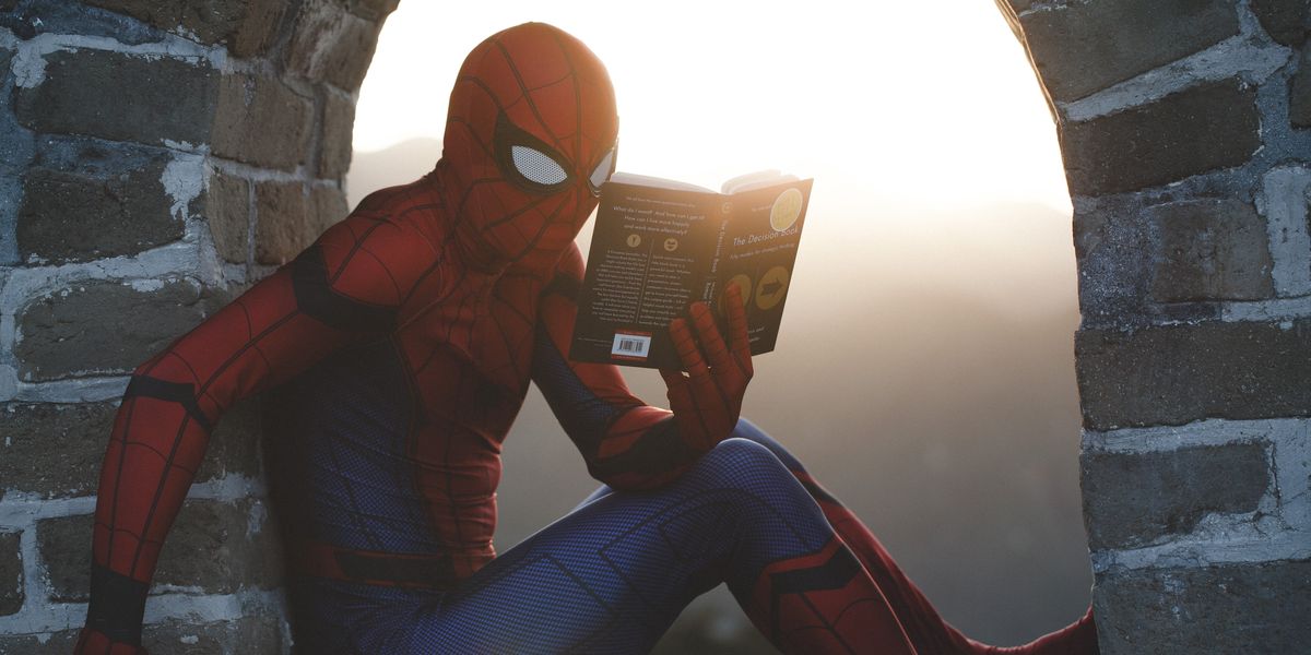 Spider-Man leaning on concrete brick while reading book