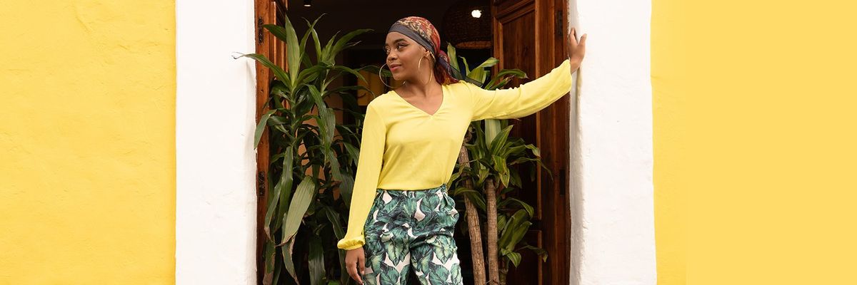 a dark-skinned Latina woman with a yellow blouse and big hoop earrings standing on a door frame