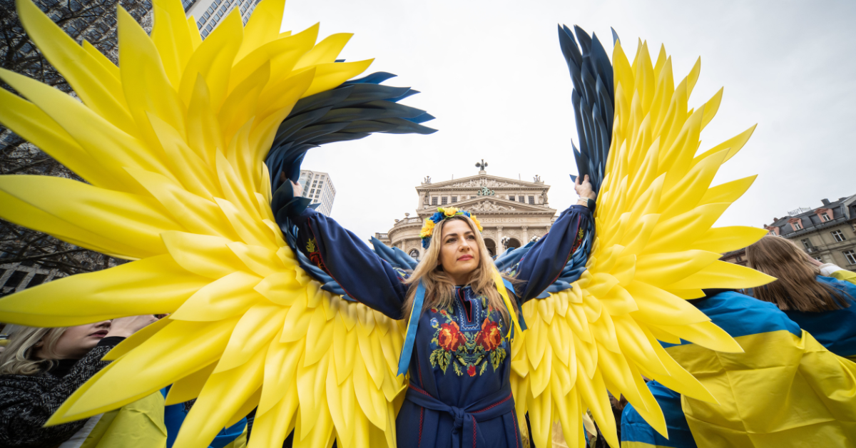 A woman with angel wings in Ukrainian colors stands in front of the Old Opera House.