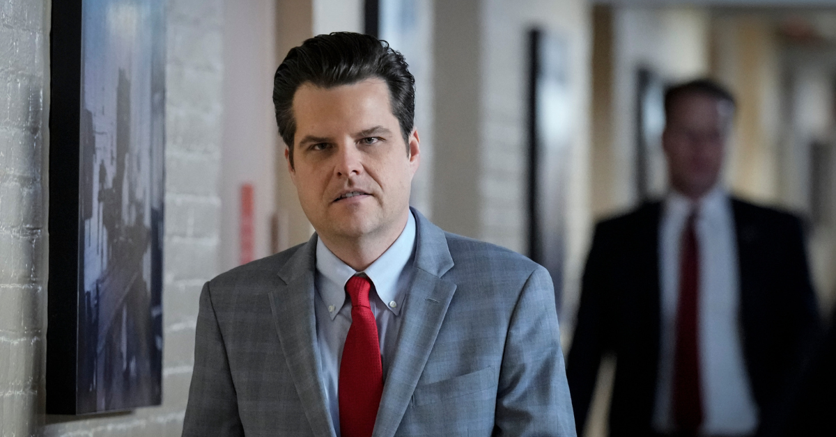 Florida Representative Matt Gaetz walking down a hallway wearing a gray suit and red tie