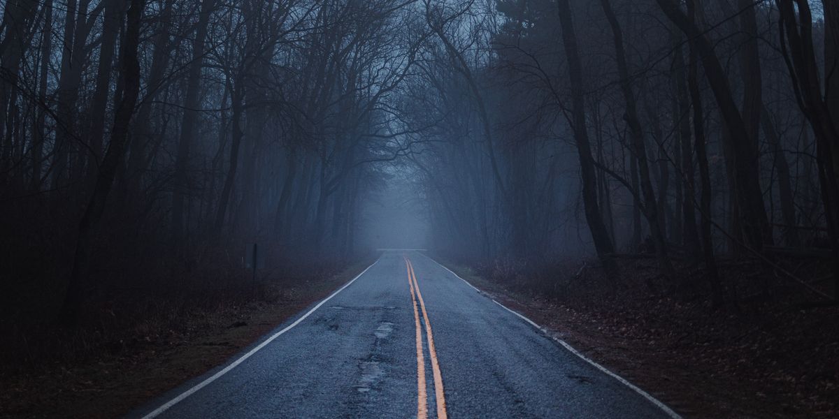 an empty road in the middle of a foggy forest