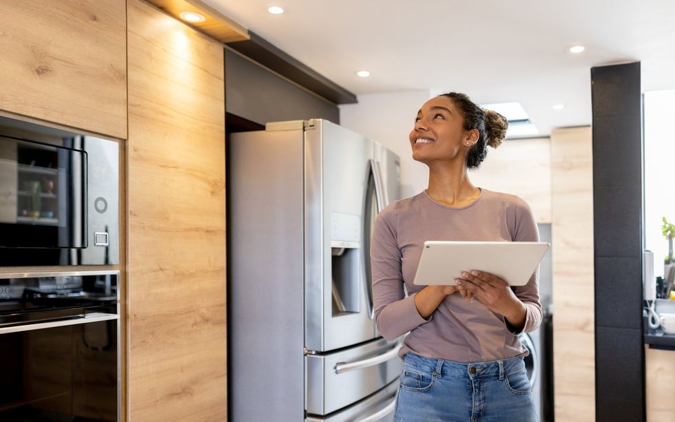a. photo of a woman in a kitchen controlling her smart devices on a tablet