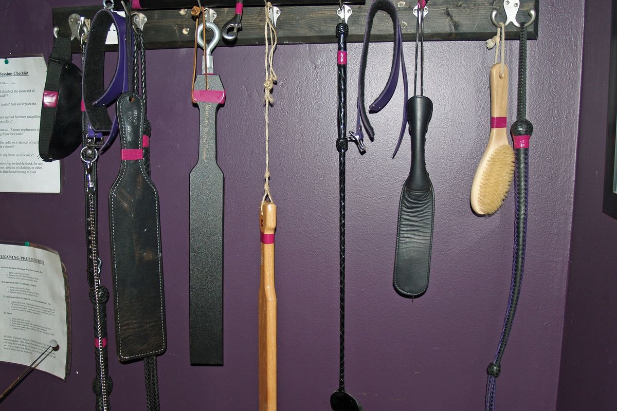 selection of paddles and riding crops hanging on a purple wall