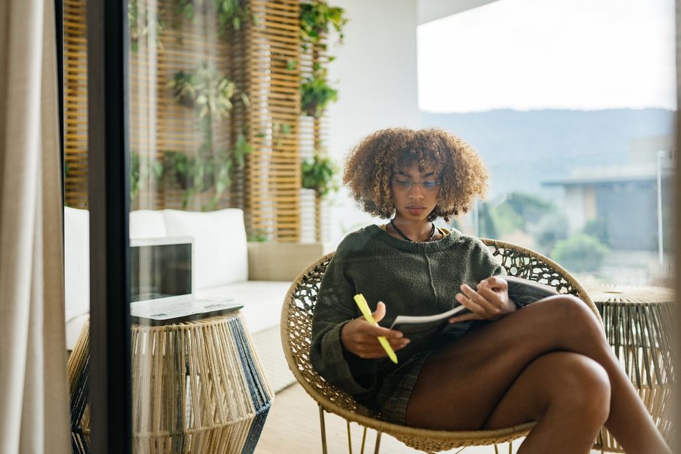 Studious-young-woman-reading-a-book-in-her-living-room-with-highlighter-in-hand