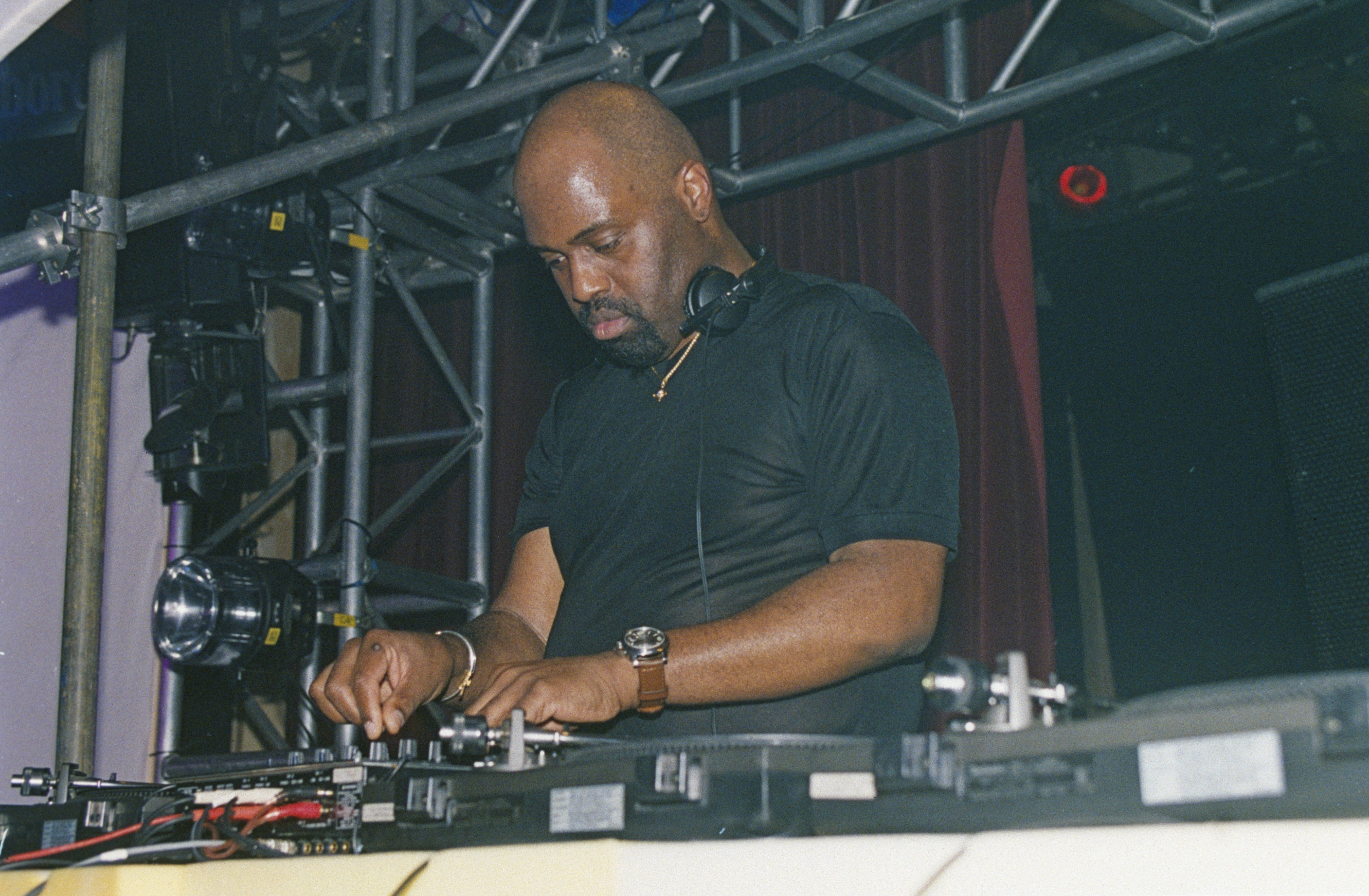 A DJ performing at a live event, focused on mixing tracks on a turntable, with a lit stage backdrop.
