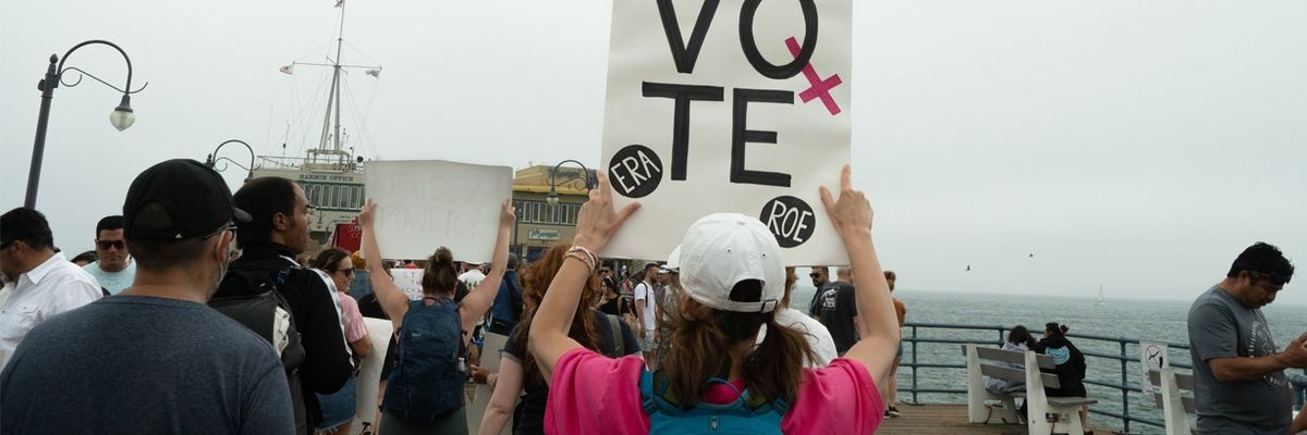 woman holds up a sign that says VOTE at a protest