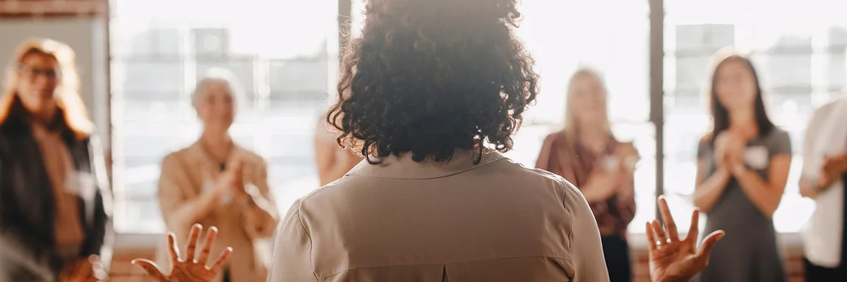 curly haired dark-skinned woman speaking to a diverse group of women