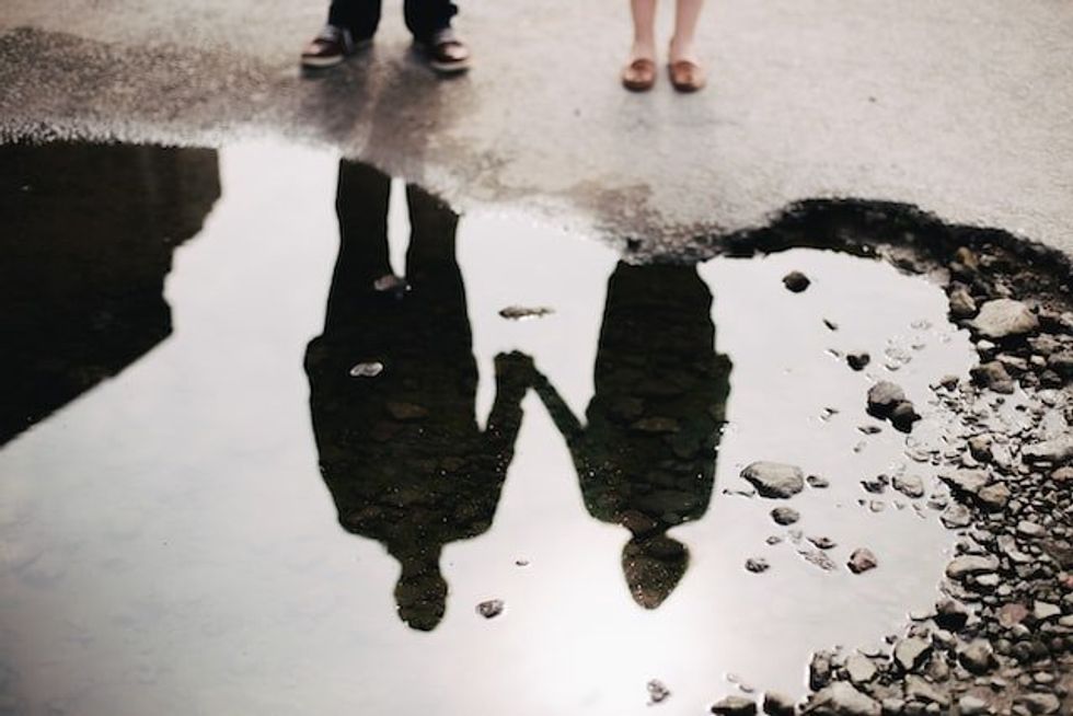 A couple reflected in a puddle holding hands