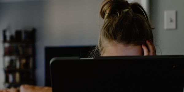 Woman with her head in her hands behind a laptop comuputer.