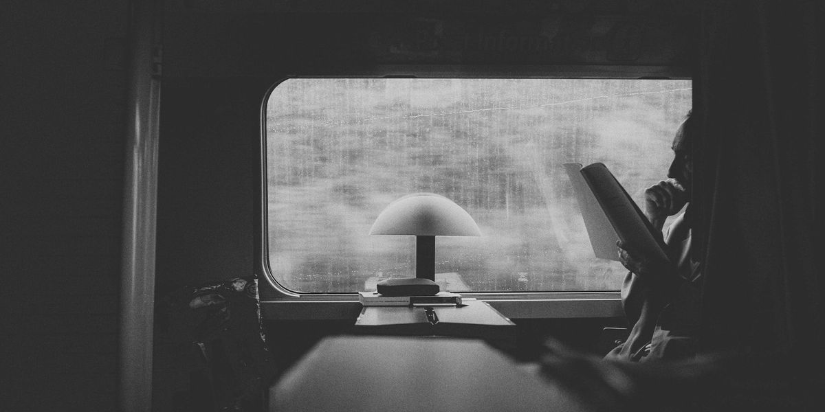 A black and white shot of a man on a train reading