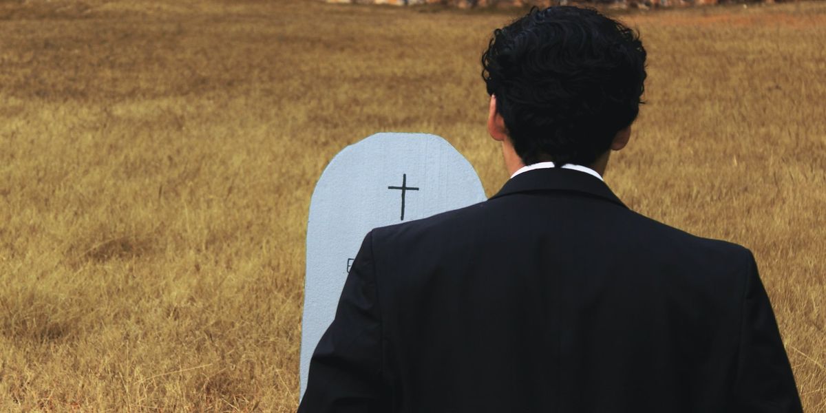 A man in a tux stands in front of a grave in a field of grass