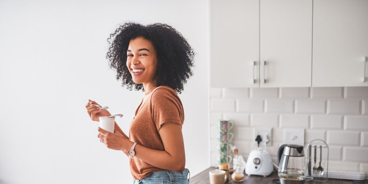black-woman-smiling-eating-yogurt-sitting-on-kitchen-table