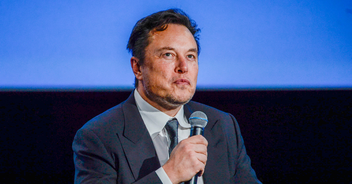 Elon Musk seated and holding a microphone