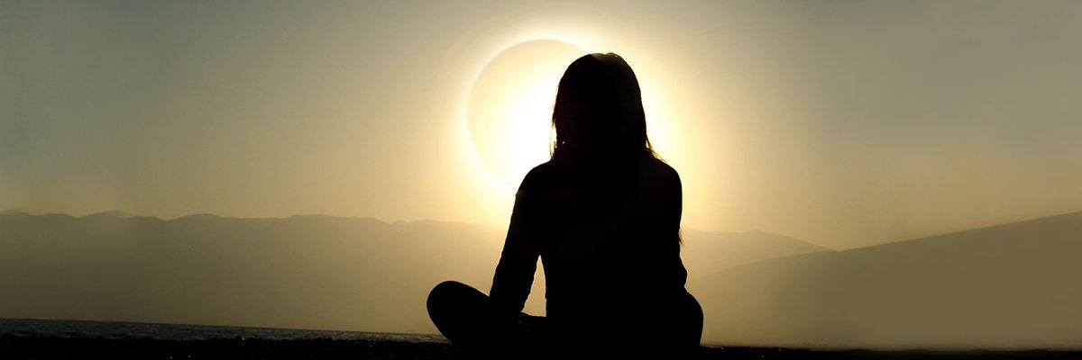 silhouette of a cross-legged woman facing a solar eclipse