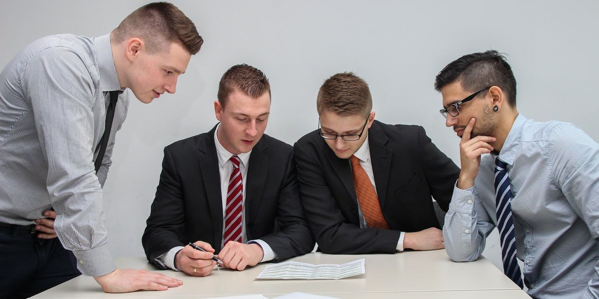 Four men in a boardroom read over a document 
