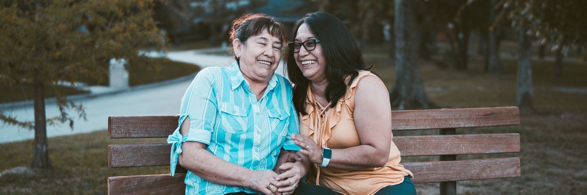 adult daughter and mother laughing on a park bench