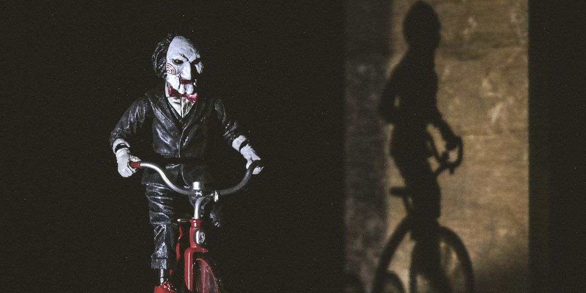 The frightening clown villain from SAW rides a red bike while their shadow follows