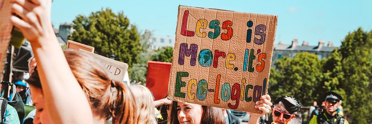 girl holding up a cardboard sign that says: less is more, it's eco-logical